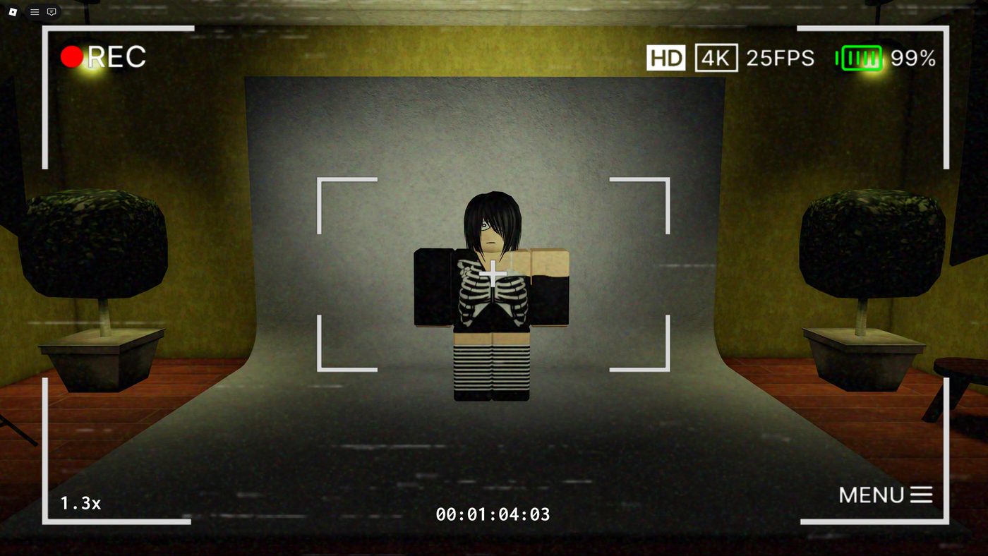 In-game footage framed as a camera viewfinder, recording a character against a studio backdrop.